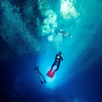 Plongeur dans le Cenote El Pit — rayons de lumière solaire traversant l'eau bleue profonde, effets de halocline visibles
