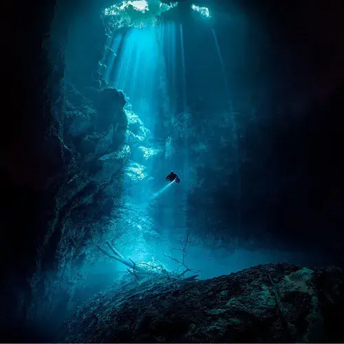 Plongée dans le cenote The Pit (El Pit) — rayon de lumière naturelle traversant l'eau cristalline vers les profondeurs, effet visuel emblématique
